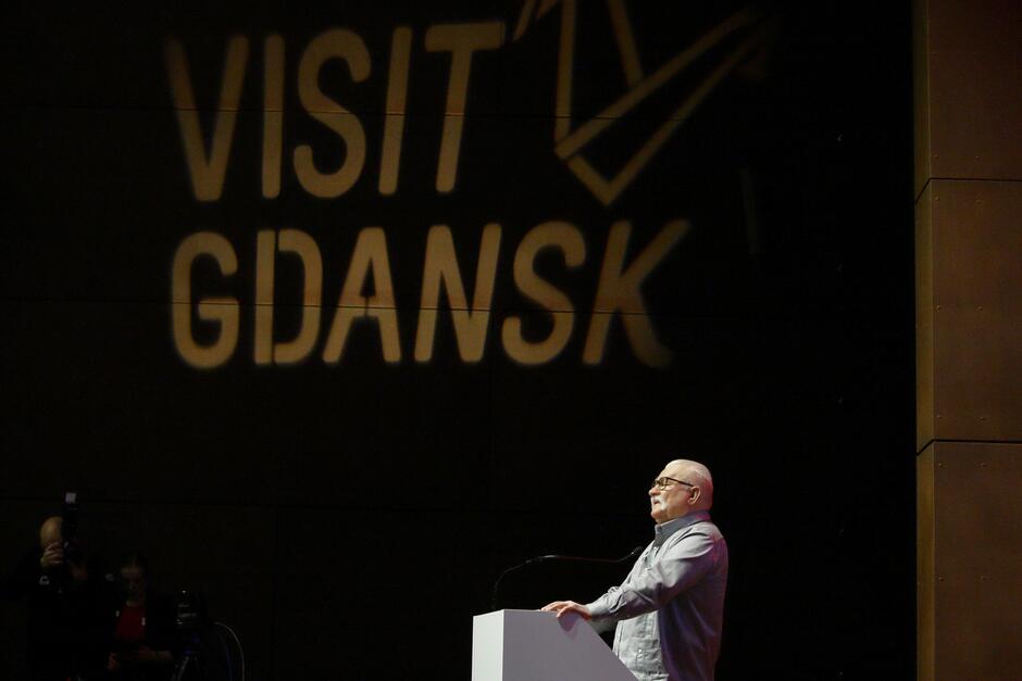 Mężczyzna przemawiający ze sceny, w tle napis Visit Gdańsk