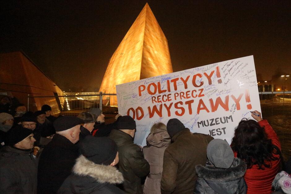 Grupa osób przed gmachem Muzeum II Wojny Światowej z transparentem Politycy! Ręce precz od wystawy!