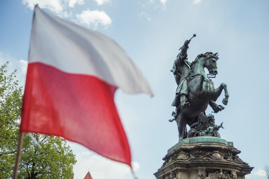 Na zdjęciu flaga biało-czerwona i pomnik jeźdźca na koniu