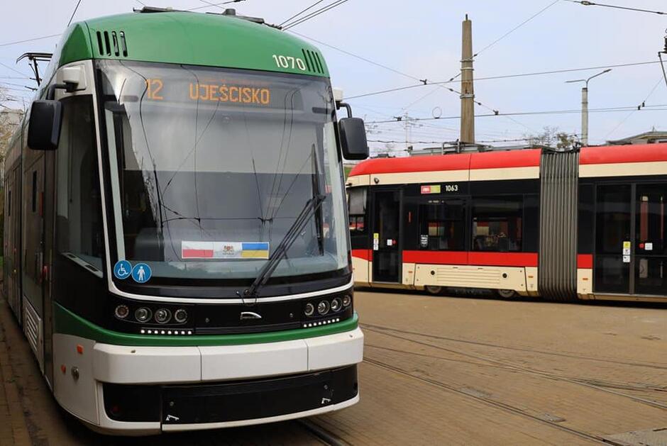 na zdjęciu biało- zielony tramwaj miejski, widać numer linii, a na przedniej szybie zawieszony szali z flagami polski i ukrainy