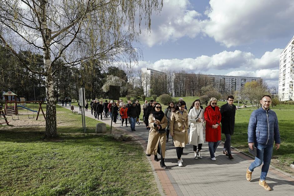 na zdjęciu grupa kilkudziesięciu osób, spaceruje chodnikiem, wokół widać zielone trawniki, a za nimi wysokie bloki mieszkalne