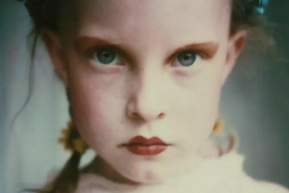 Zdjęcie kolorowe, dziewczynka z makijażem i małymi warkoczykami patrzy na wprost z poważną miną