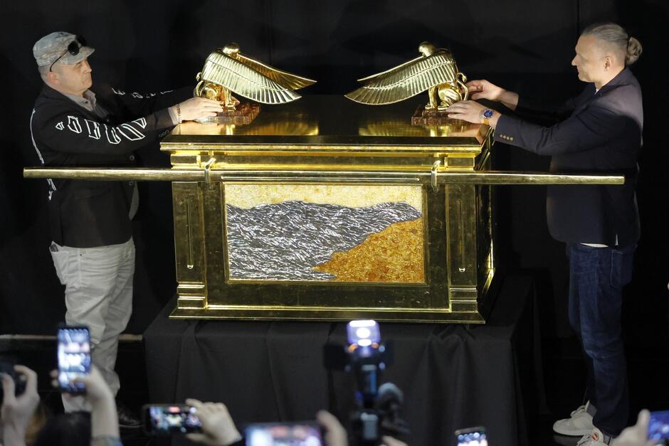 na zdjęciu ogromna bursztynowa skrzynia symbolizująca arkę przymierza, na jej pokrywie dwóch mężczyzn ustawia złote skrzydła z obu stron skrzyni