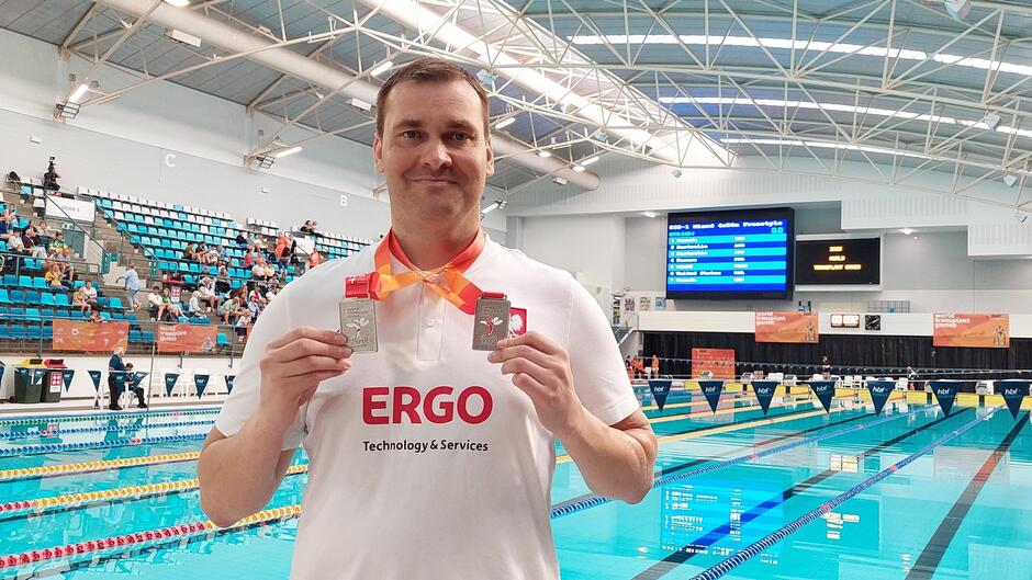 Mężczyzna w białej koszulce z dwoma medalami na szyi