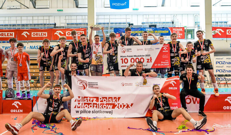 Młodzi zawodnicy siedzą i stoją na parkiecie, cieszą się