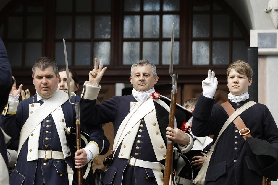 Trzej mężczyzn w stroju wojskowym z epoki w jedną ręką uniesioną do przysięgi