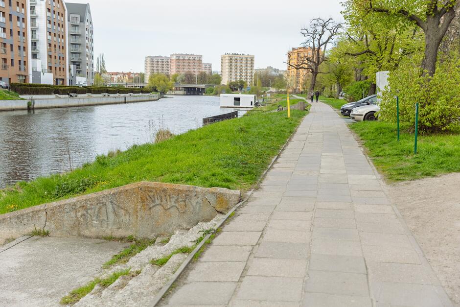 na zdjęciu fragment chodnika i schodów, po lewej widać wody rzeki Motława, a w tle kilka wysokich budynków mieszkalnych oraz hoteli