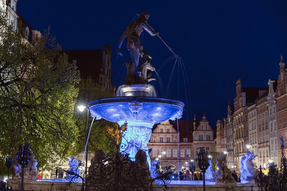 po zmroku podświetlona na niebiesko fontanna przedstawiająca mitycznego króla mórz, nagiego mężczyznę z trójzębem w dłoni 