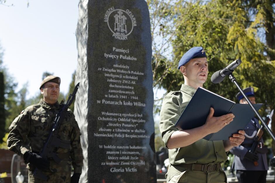 harcerz czyta tekst na tle pomnika, obok warta honorowa