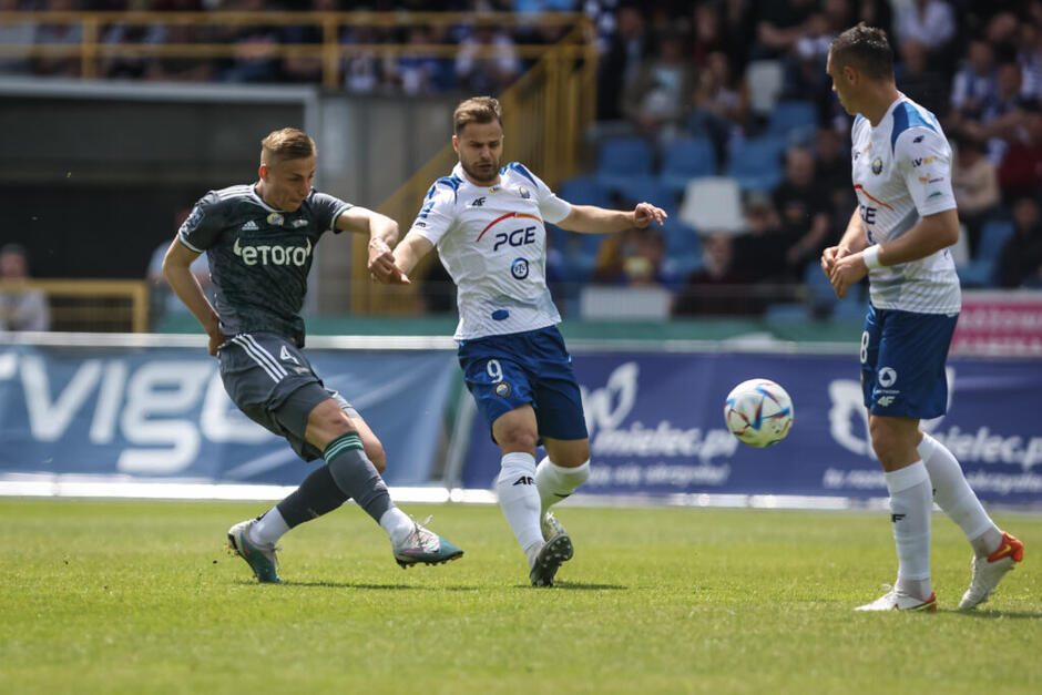 Trzech zawodników przy piłce, po lewej w szarym stroju