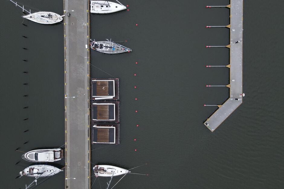 zdjęcie z drona, widać pomosty w przystani jachtowej przy których zacumowanych jest kilka łodzi