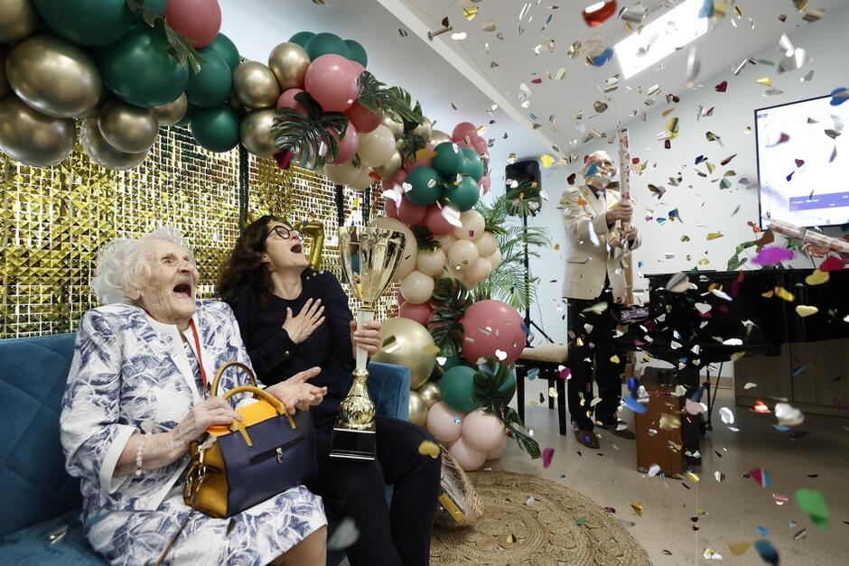 seniorka i prezydentka na sofie, patrzą w górę na wystrzelone konfetti