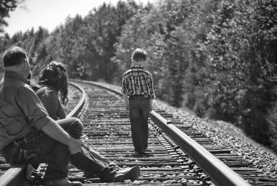 Czarno-białe zdjęcie: chłopiec odwrócony plecami na torach kolejowych 