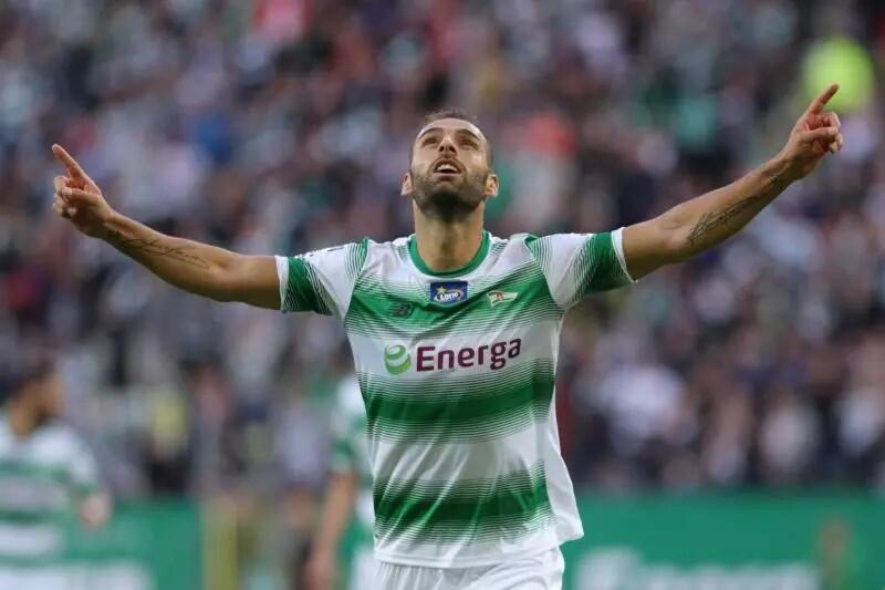 Mężczyzna w biało-zielonej koszulce: ręce uniesione do góry, głowa zadarta do góry