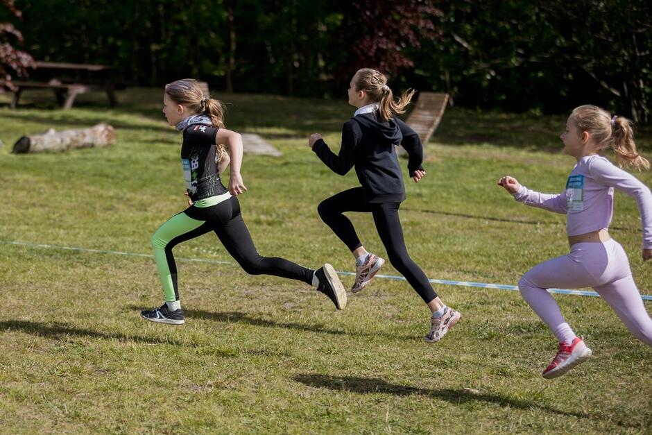 trzy dziewczynki w strojach sportowych biegną po trawie