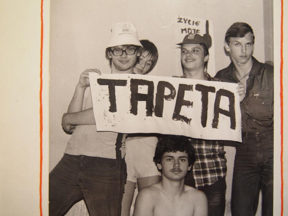 czarno-białe zdjęcie, pięciu młodych mężczyzn pozuje z banerem z napisem tapeta