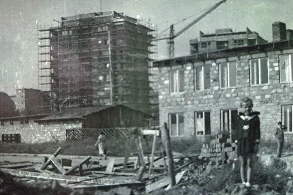 Czarno-białe zdjęcie pokazujące budowę szkoły, na pierwszym planie stoi dziewczynka