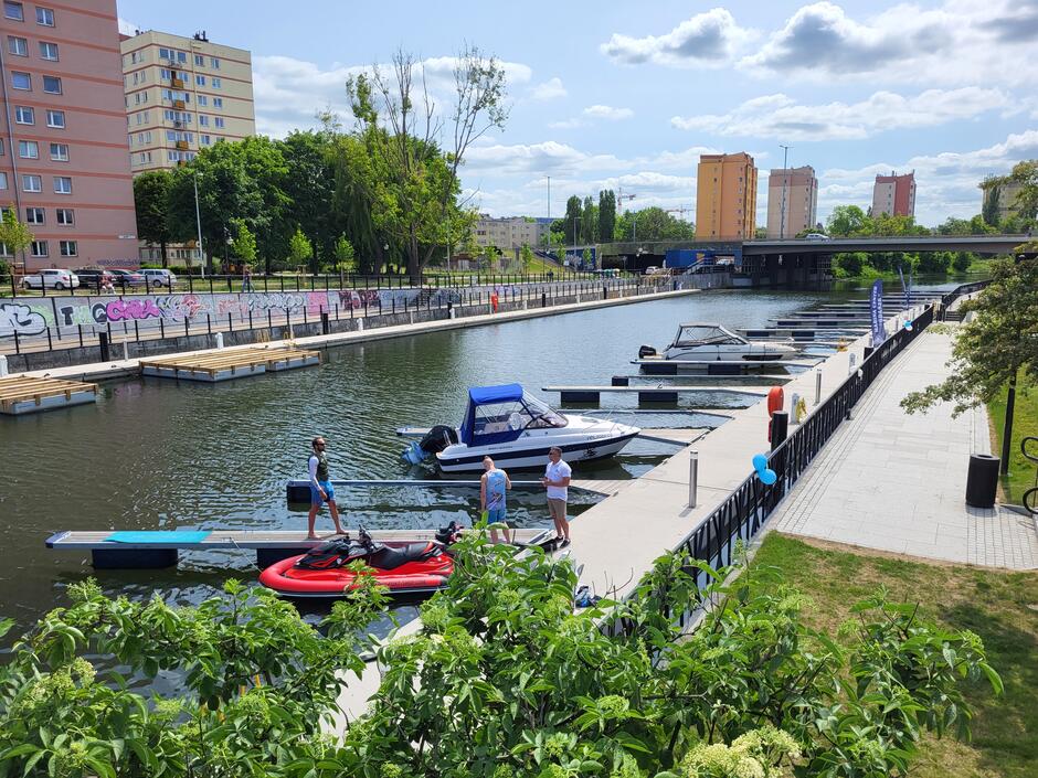 na zdjęciu nowa marina, widać pomosty i kilka zacumowanych małych łódek na rzece, w tle kilka budynków mieszkalnych