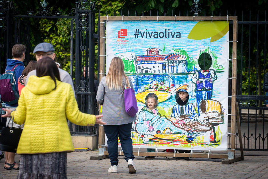 Kilka osób (tyłem do obiektywu) patrzą na kolorowy obraz z napisem Viva Oliwa
