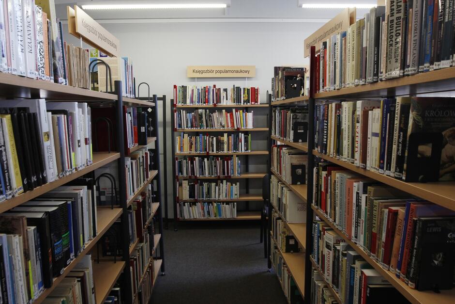 na zdjęciu kilka regałów w bibliotece, szczelnie wypełnione różnego rodzaju książkami