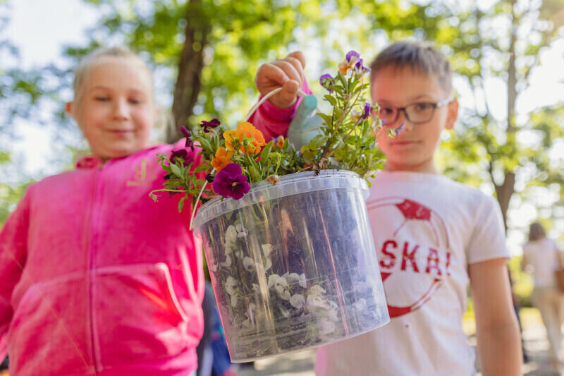 Dwoje dzieci trzyma pojemnik plastikowy a w nim kwiaty