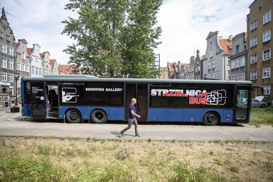 na zdjęciu duży niebieski autokar z napisem strzelnica bus, obok niego przechodzi mężczyzna