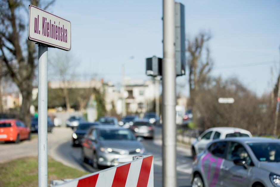 na zdjęciu fragment ulicy która gęsto jedzie kilkanaście samochodów jeden za drugim, po lewej na pierwszym planie widać też tabliczkę z nazwą ulicy Kielnieńska