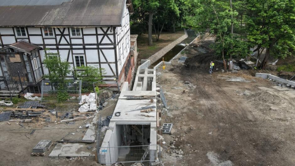 na zdjęciu budowla techniczna betonowa, obok widać zabytkowy dom w jasnych barwach