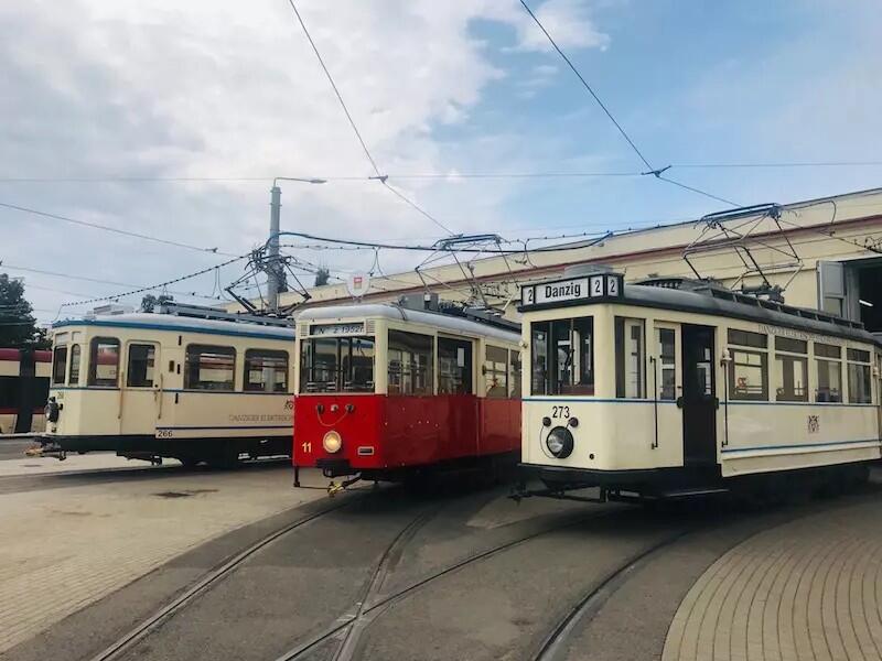 Trzy starodawne tramwaje stoją na torach: białe po bokach, w środku czerwony