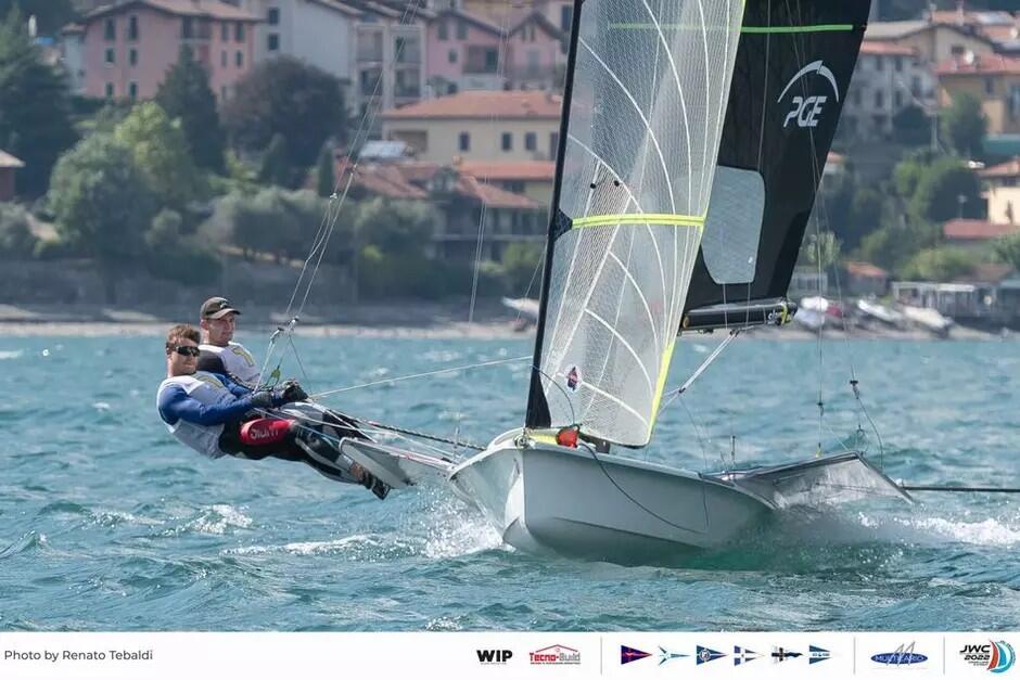 Dwóch żeglarzy na łódce z żaglem, są poza łódką prawie na leżąco, trzymają linki