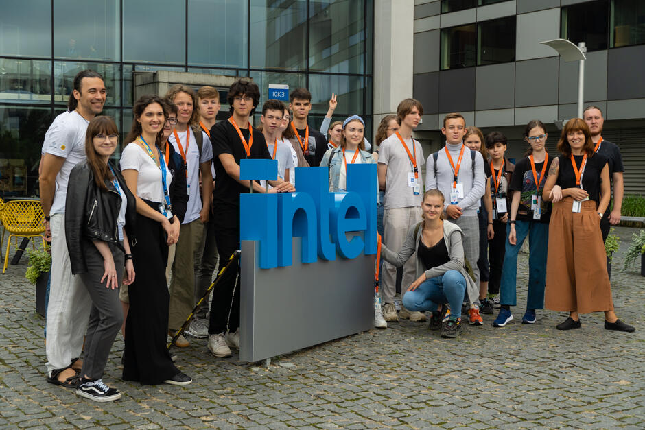 młodzież stoi wokół wielkiego logo firmy Intel, przed budynkiem