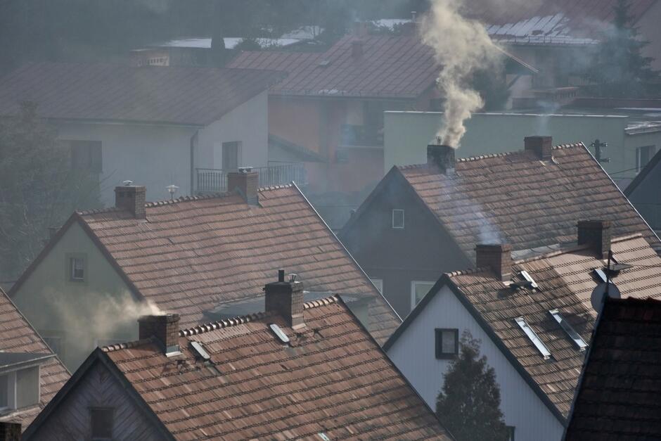 Dachy domów z kominami, z których wylatuje dym
