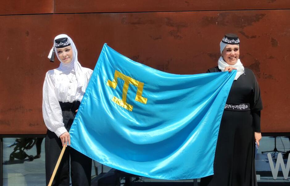 kobiety w strojach tatarskich tradycyjnych rozwijają błękitną flagę