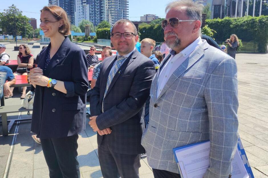 Kobieta i dwóch mężczyzn w średnim wieku stoją na nasłonecznionym placu