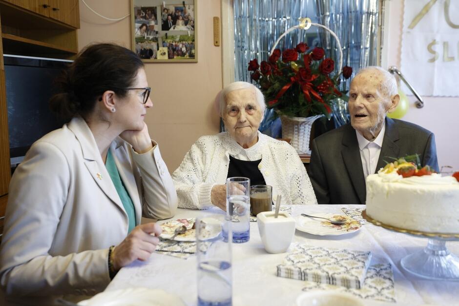 para seniorów siedzi przy stole, obok nich prezydent
