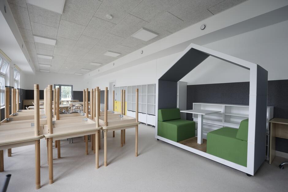 na zdjęciu sala lekcyjna, widać ławki i krzesełka, a także konstrukcję w formie domku w którym umieszczono zielone pufy i stolik pomiędzy nimi