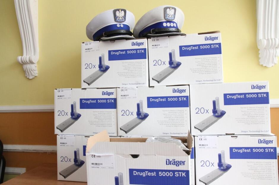 Pudełka z napisem drugtest ustawione jedno na drugim a na nich położono dwie policyjne czapki