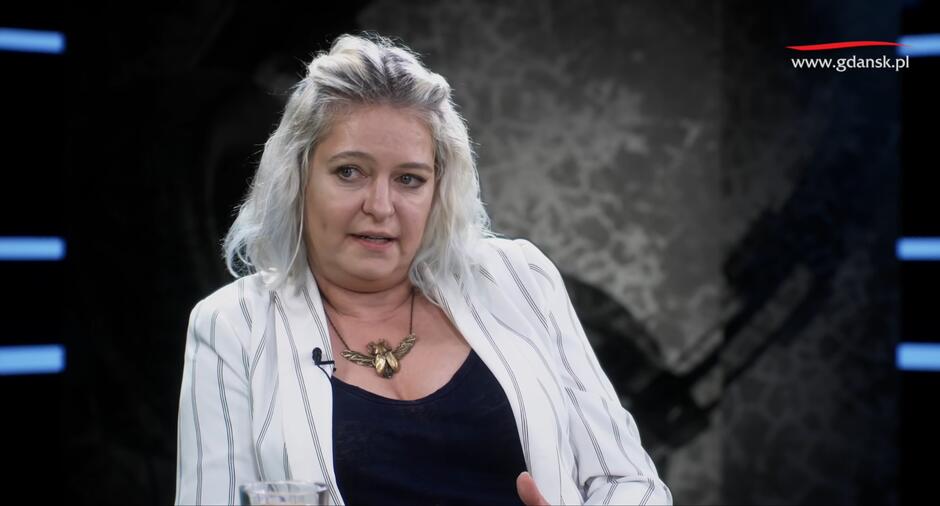 blondynka w średnim wieku w białej marynarce, w studiu nagraniowym, mówi