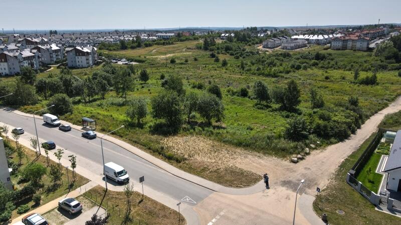 Widok z góry: rondo i skrzyżowanie drogi asfaltowej z piaszczystą. U góry zieleń, drzewa, trawniki 