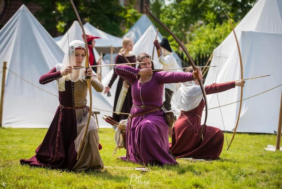 łuczniczki na trawniku, w tle białe namioty