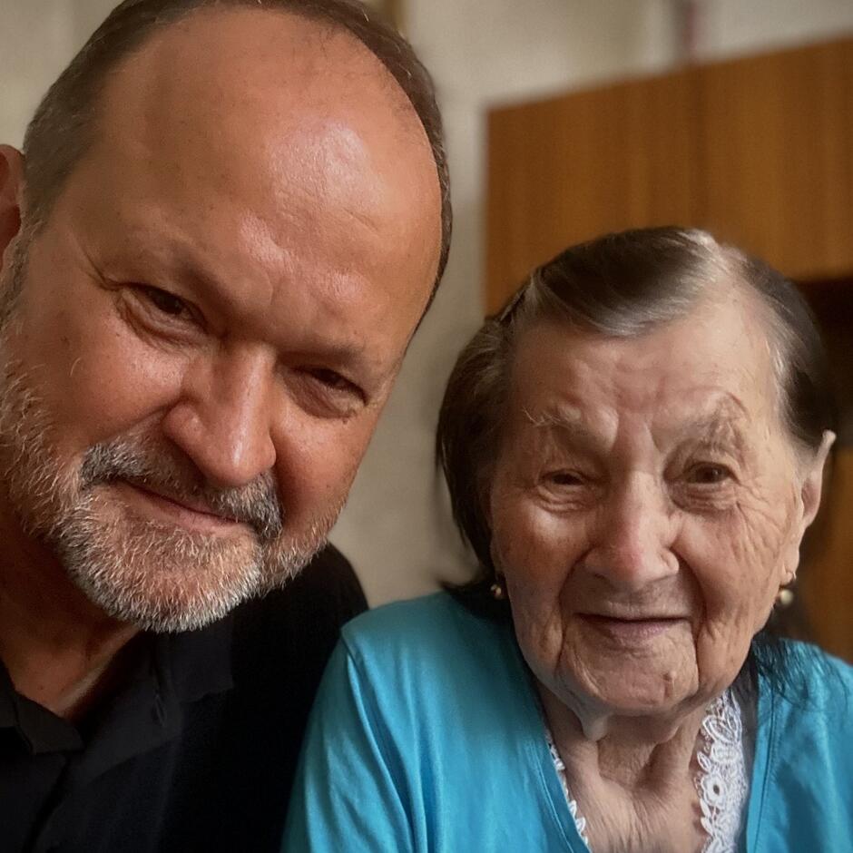 Zdjęcie przedstawia dwie osoby, głowa przy głowie, patrzące w stronę obiektywu aparatu fotograficznego. Po lewej łysawy mężczyzna po sześćdziesiątce, po prawej sędziwa kobieta o siwych włosach 