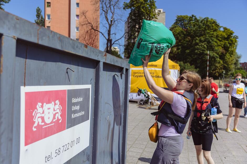 kobieta w kapoku wrzuca worek ze śmieciami do kontenera