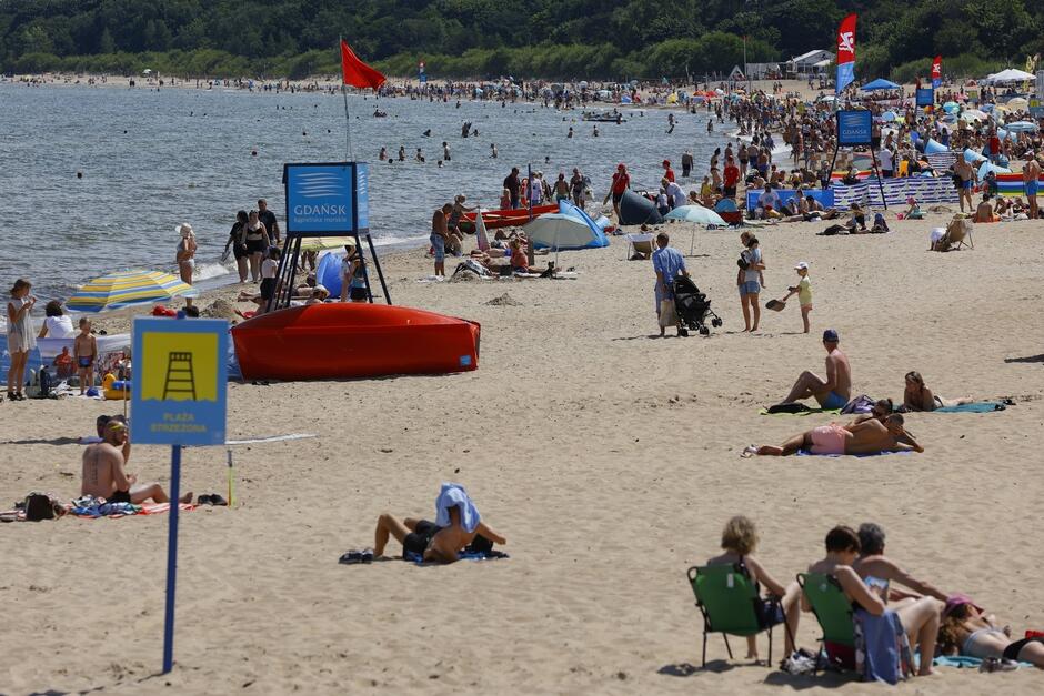 Zapełniona ludźmi plaża morska, na której widać czerwone flagi