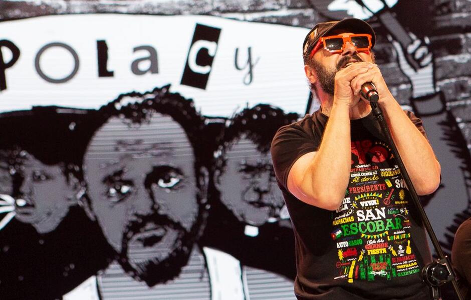 wokalista w ciemnych okularach przy mikrofonie, za nim w tle ogroman namalowana twarz