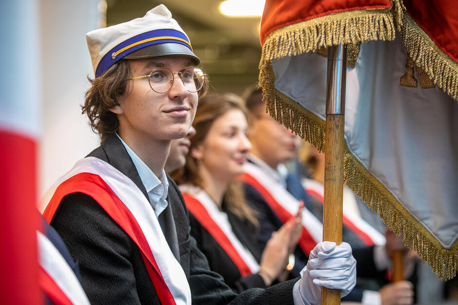 Młody człowiek w okularach i czapeczce typu rogatywka, uśmiecha się