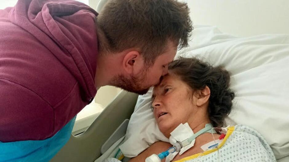 Młody mężczyzna całujący w czoło kobietę leżącą na łóżku szpitalnym