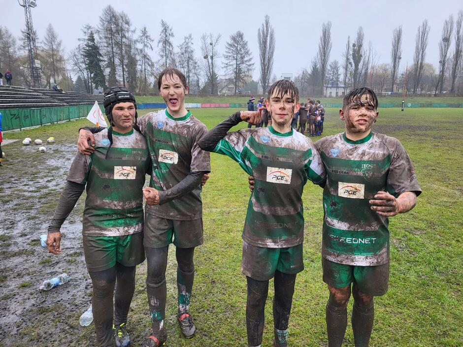 Czterech chłopaków na murawie w zielonych strojach umorusanych w błocie
