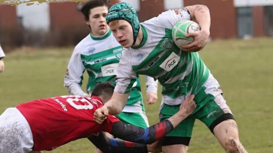 Dwóch młodych rugbistów walczy o piłkę. Mają kaski ochronne na głowach 