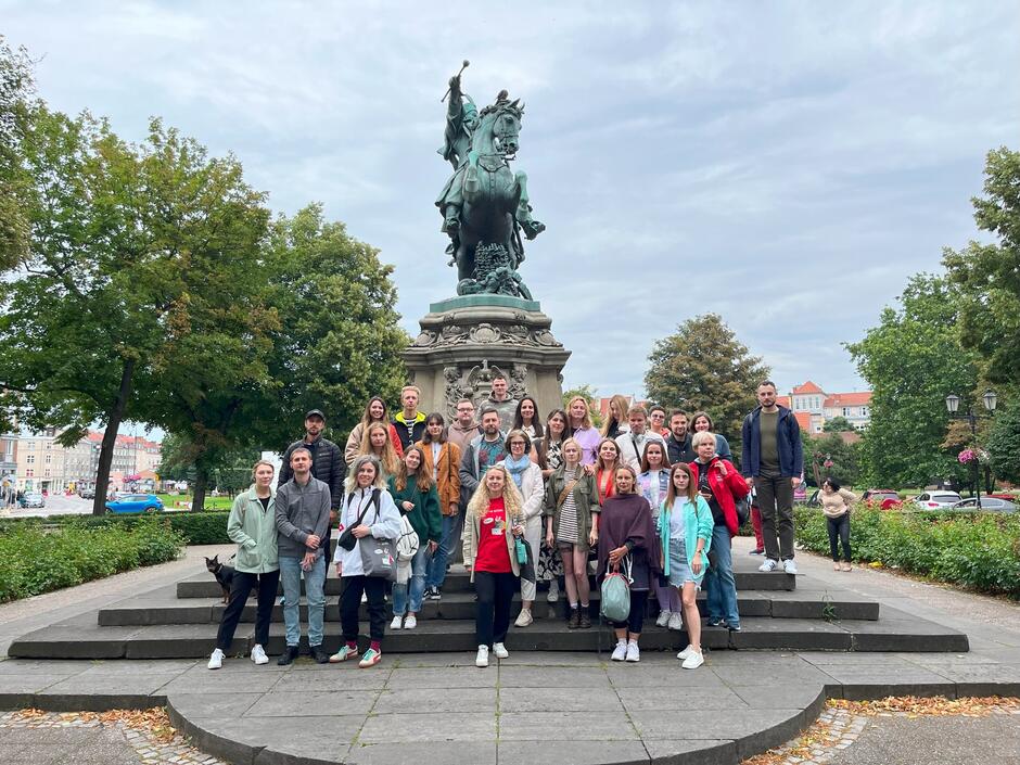 Grupa ludzi pod pomnikiem człowieka na koniu