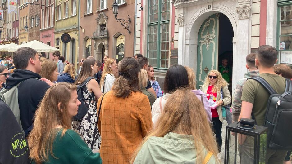 Kilkanaście osób na ulicy, w tle kamienica 